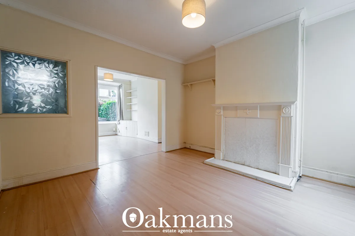 Spacious living room with wooden flooring, cream walls, ceiling light fixture, framed artwork, fireplace with mantelpiec