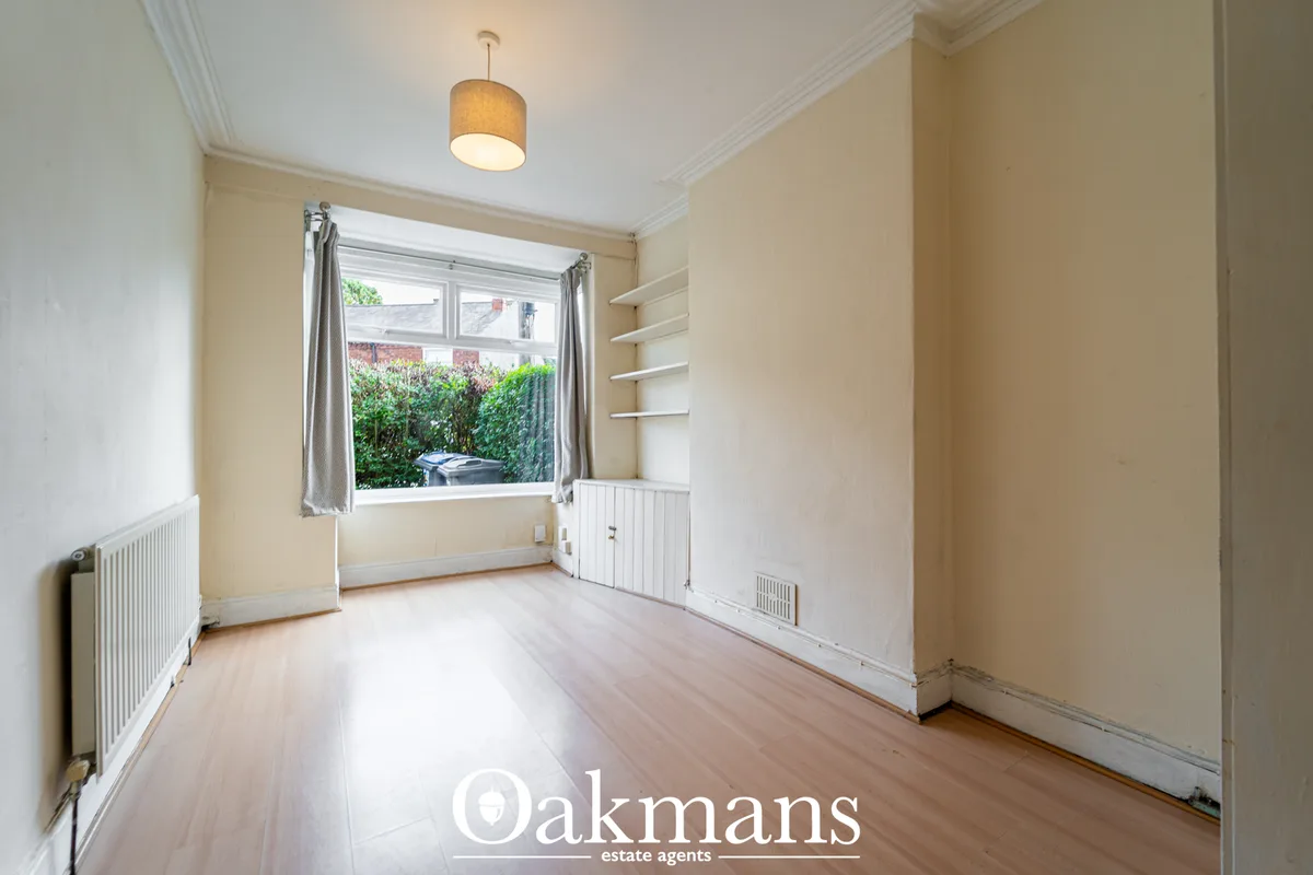 Bright bedroom with wooden flooring, cream walls, radiator heating, wall-mounted shelving, and large window overlooking 
