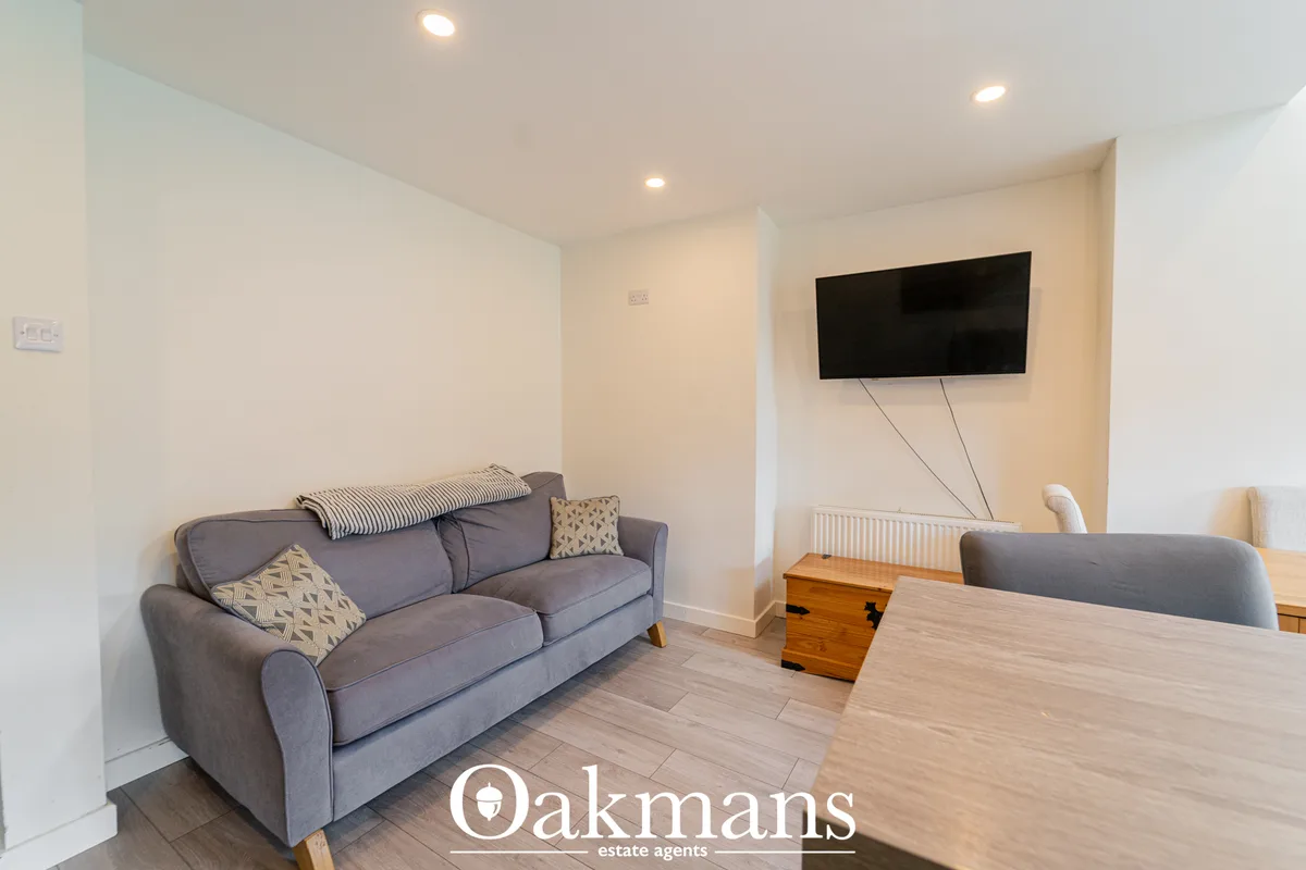 Modern living room with grey upholstered sofa, wooden floor, wall-mounted flat-screen TV, recessed ceiling lights and wh