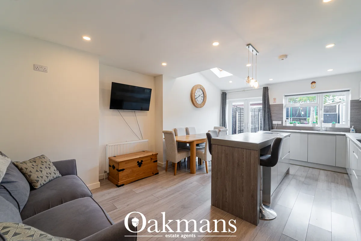 Open-plan living room with grey sofa, wooden chest, wall-mounted TV, dining table, and kitchen area with island, large w