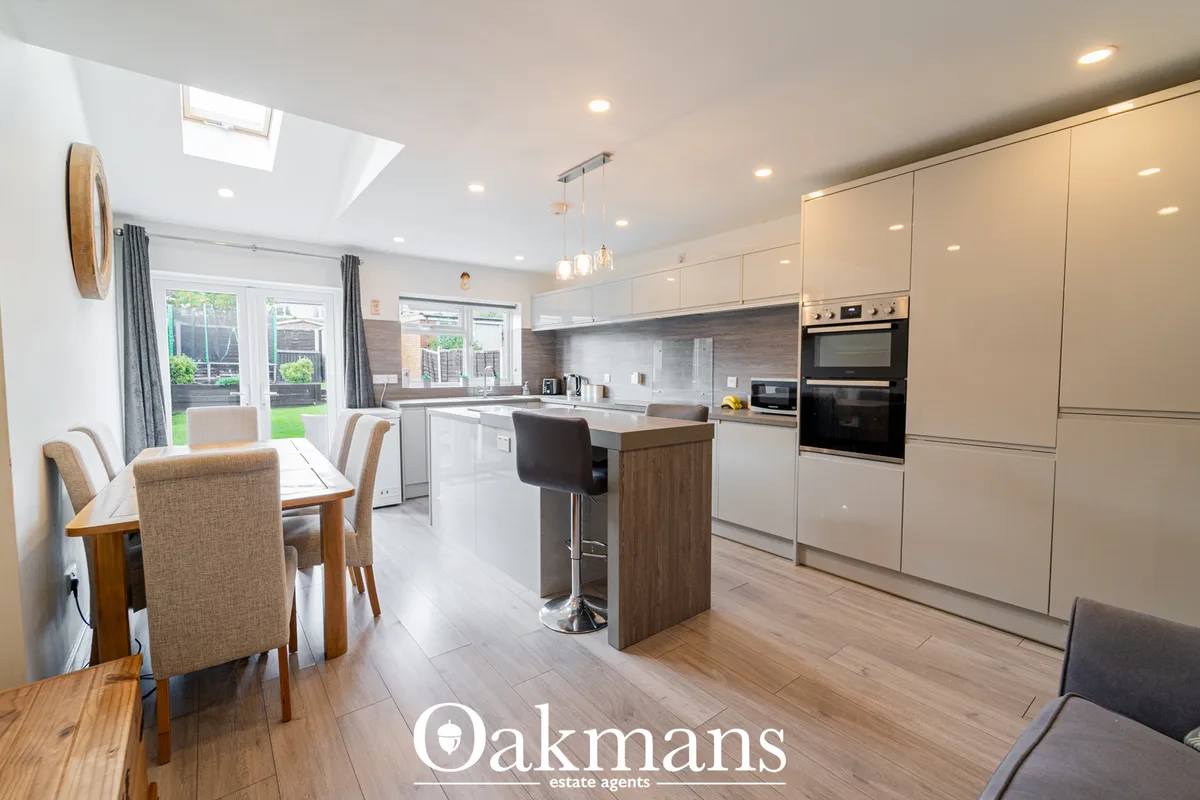 Modern open-plan kitchen with cream units, wood-effect breakfast bar, integrated appliances, and dining area with garden
