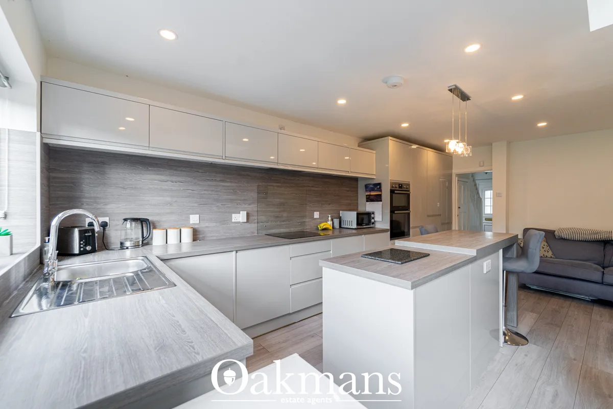 Modern fitted kitchen with white units, dark wood backsplash, grey stone worktops, island with breakfast bar, integrated