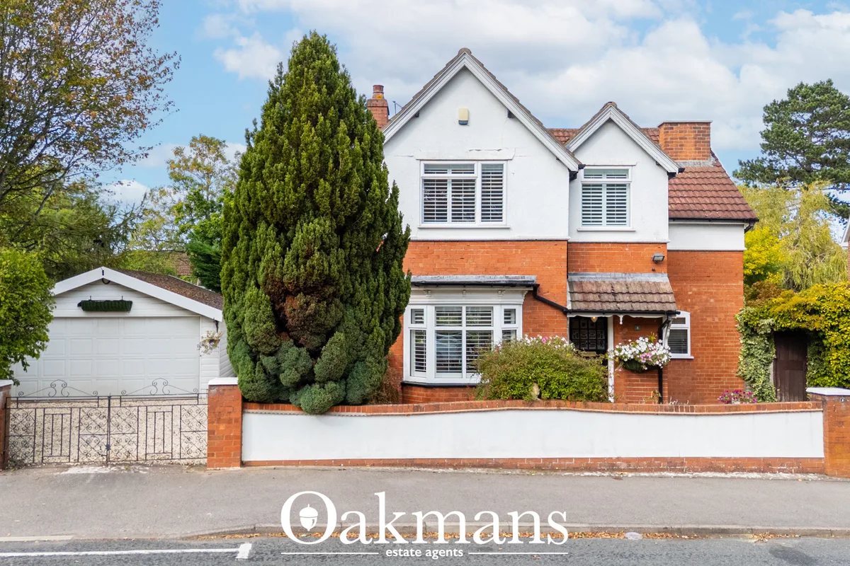 Two-storey brick and white rendered family home with pitched roof, front garage, boundary wall and mature trees