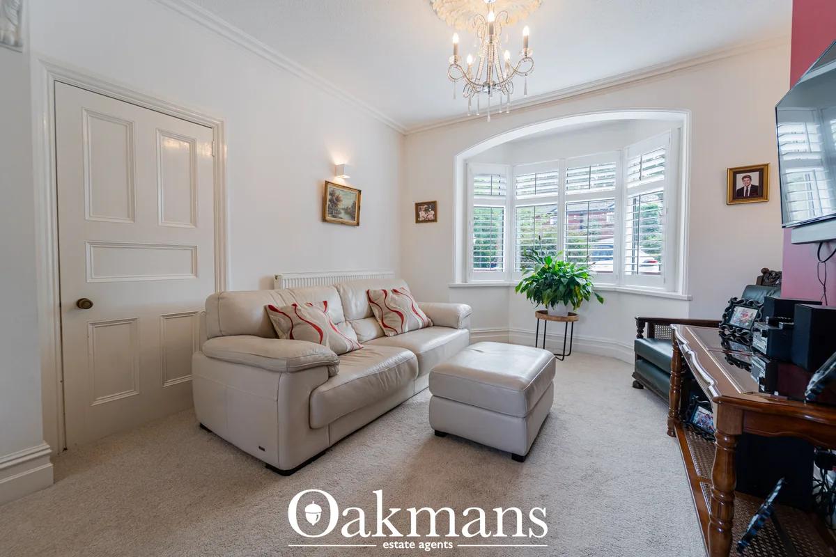 Elegant living room with cream upholstered sofa, matching ottoman, decorative cushions, crystal chandelier, white shutte