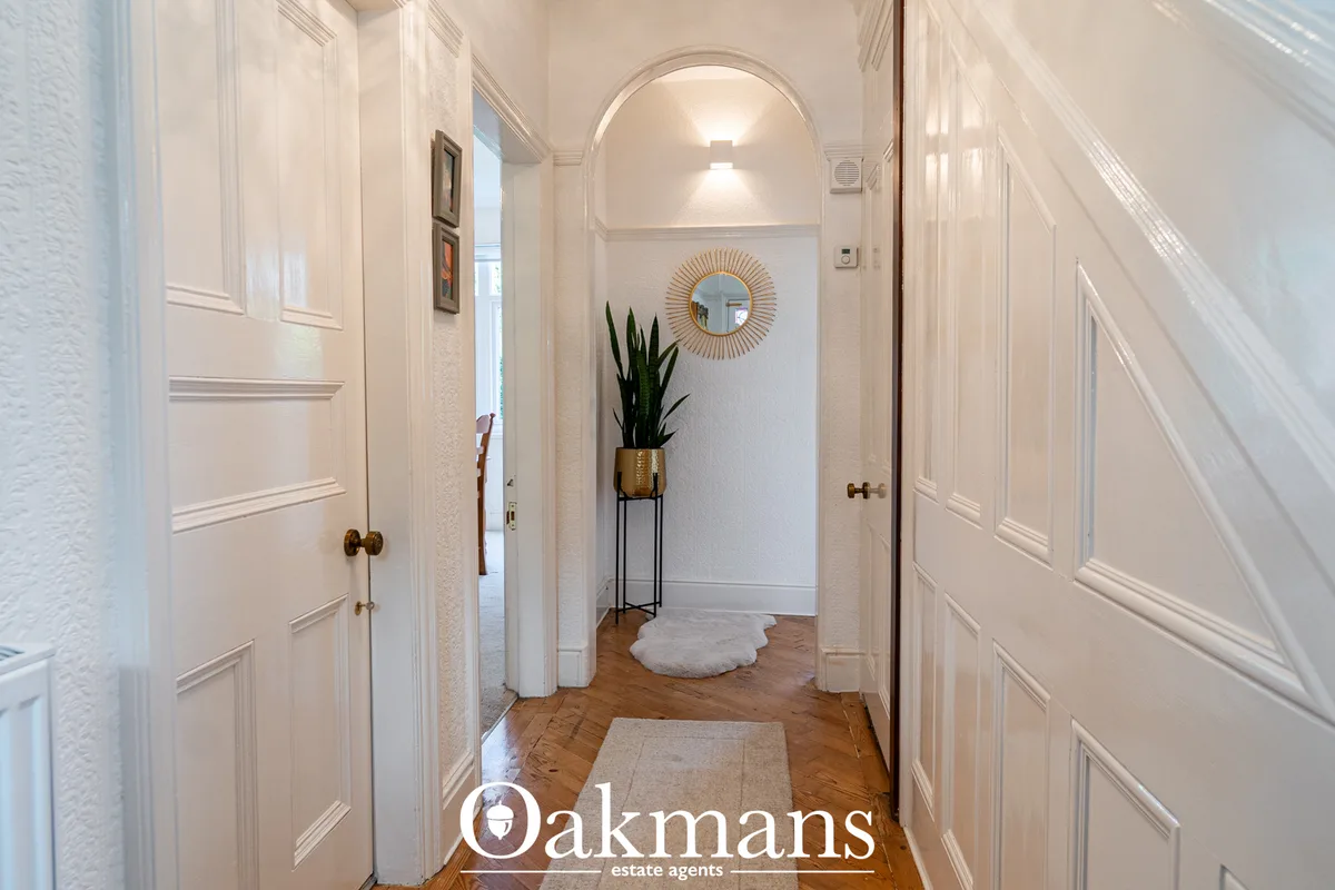 Bright hallway with cream walls, white panelled doors, arched doorway, potted plant on stand, sunburst mirror and wooden