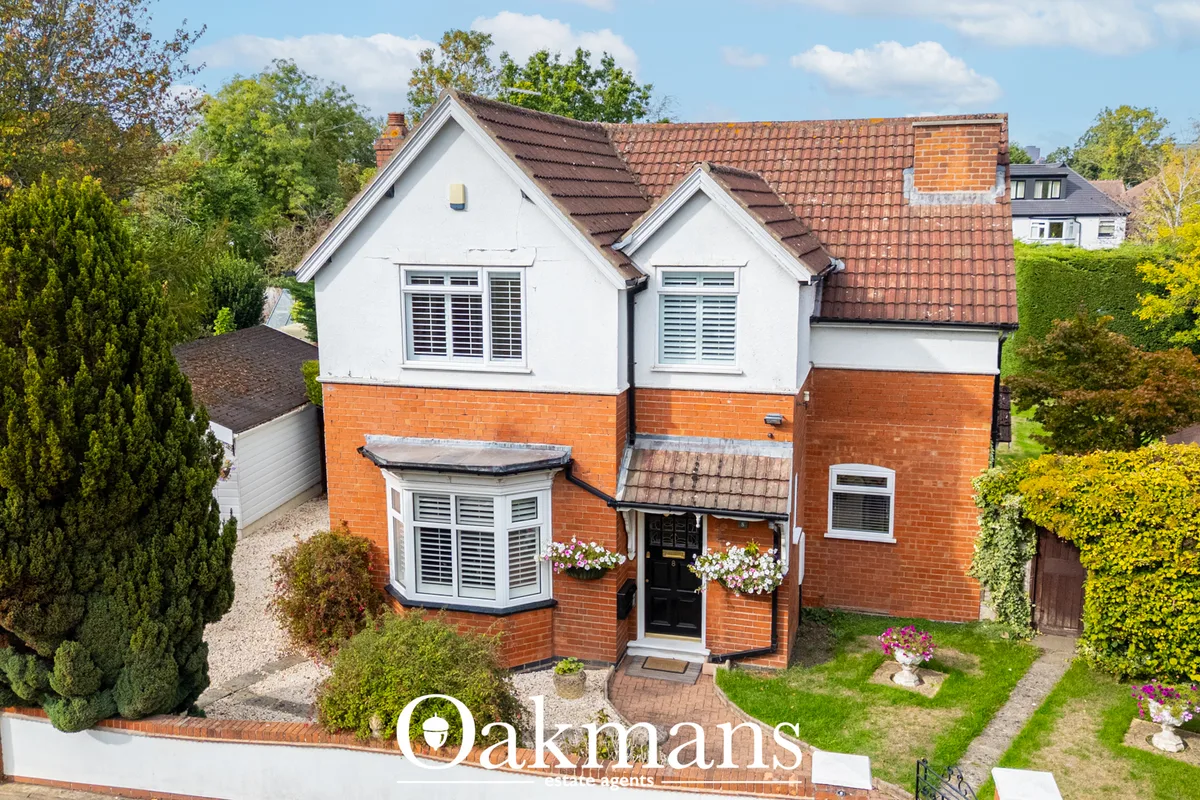 Detached two-storey brick and white rendered house with tiled roof, bay window, black front door, flowering baskets, nea