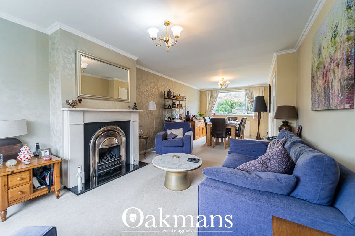 Spacious living room with blue sofa, fireplace with ornate mantelpiece and mirror, wooden furniture, brass chandelier an