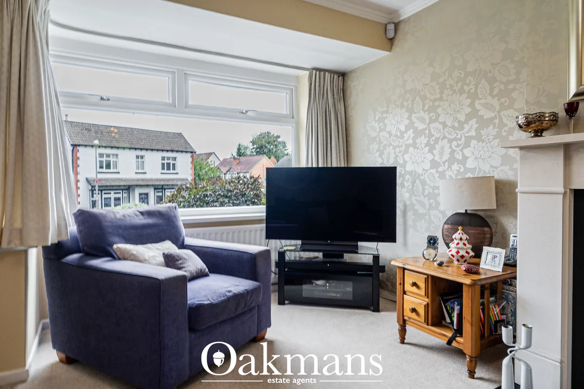 Bright living room with navy armchair, flat-screen TV on stand, wooden side table, and large bay windows overlooking sub