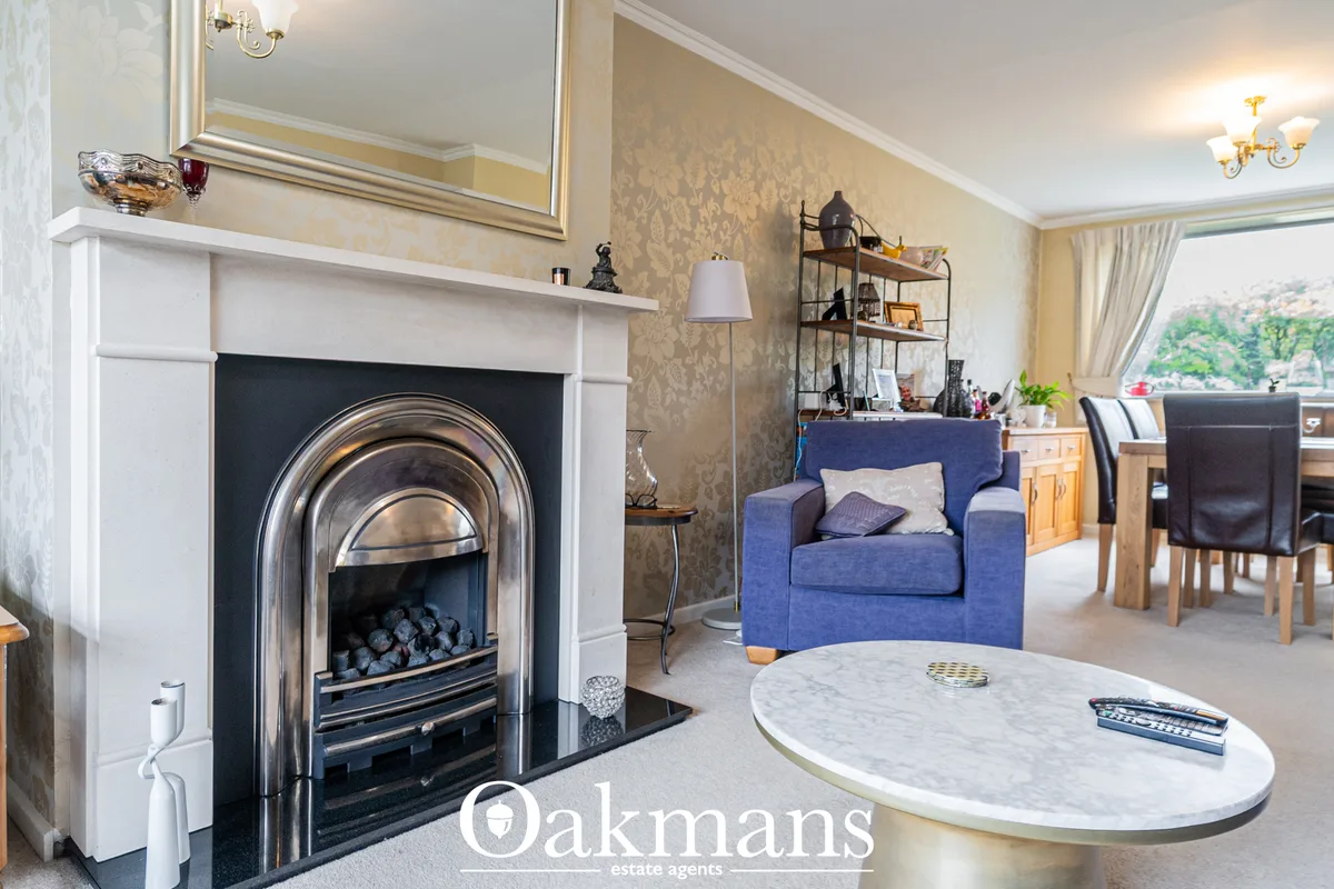Elegant living room with white fireplace, blue armchair, marble coffee table, patterned wallpaper and windows overlookin