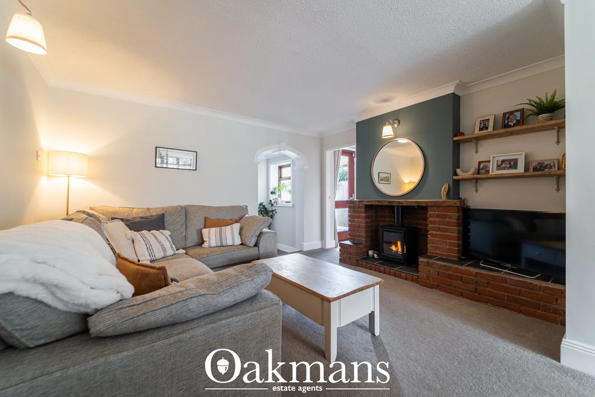 Spacious living room with grey sofa, fireplace with red brick surround, round mirror, wooden shelving, TV, and access to