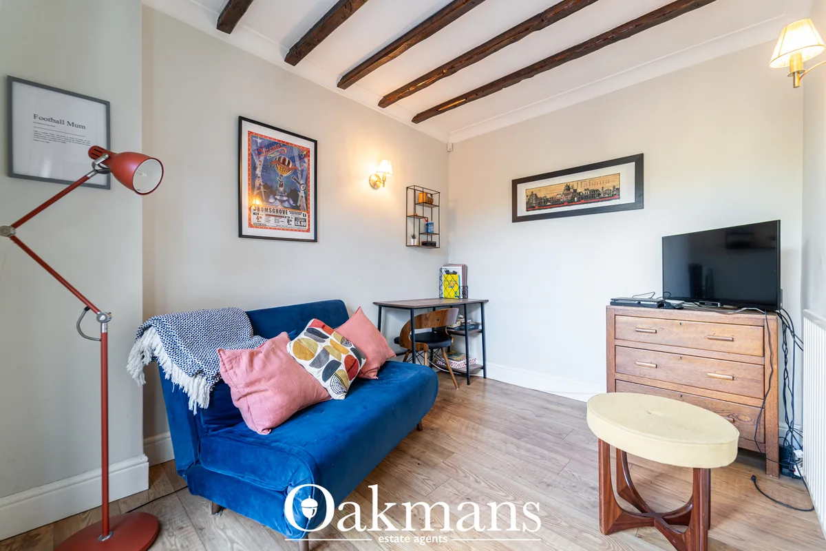 Living room with blue sofa, pink cushions, wooden beams, TV on dresser, framed artwork and red floor lamp