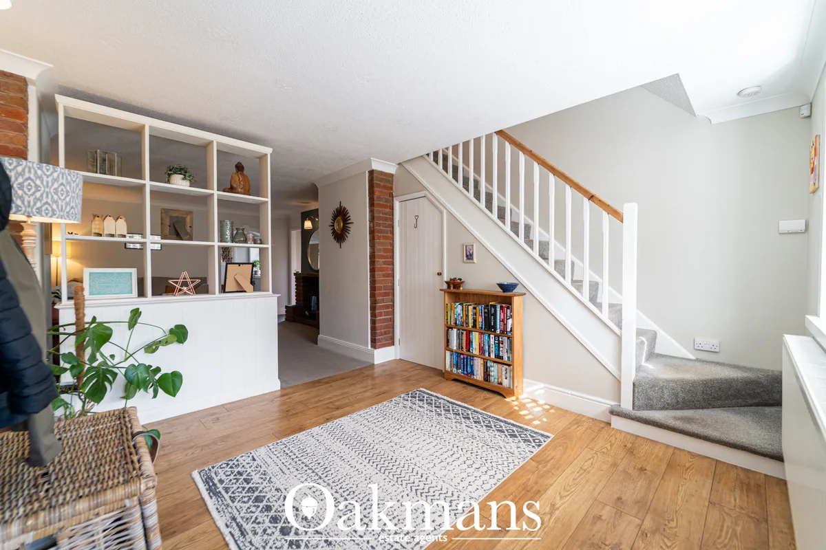 Bright entrance hallway with wooden flooring, white staircase, shelving unit, bookcase under stairs, geometric rug and e