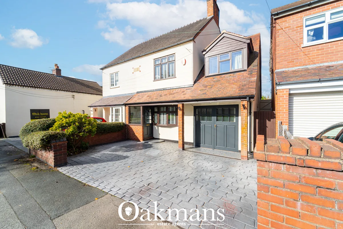 Front view of detached brick and white rendered house with grey garage door, driveway and manicured hedging, clear blue 