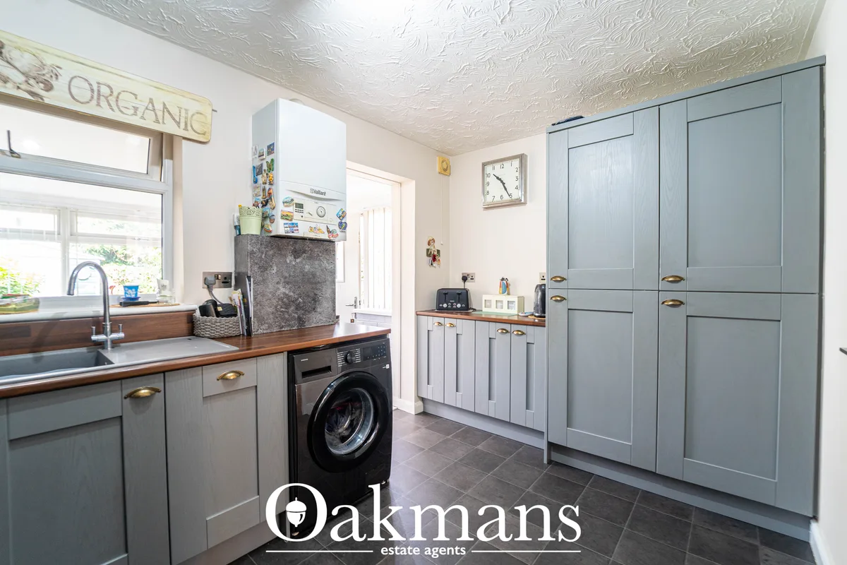 Bright utility room with grey cabinetry, washing machine, wood countertops, sink, and built-in storage cupboards
