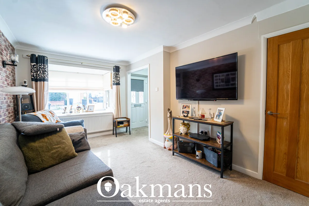 Bright living room with grey sofa, wall-mounted TV above console table, bay window with patterned curtains, exposed bric
