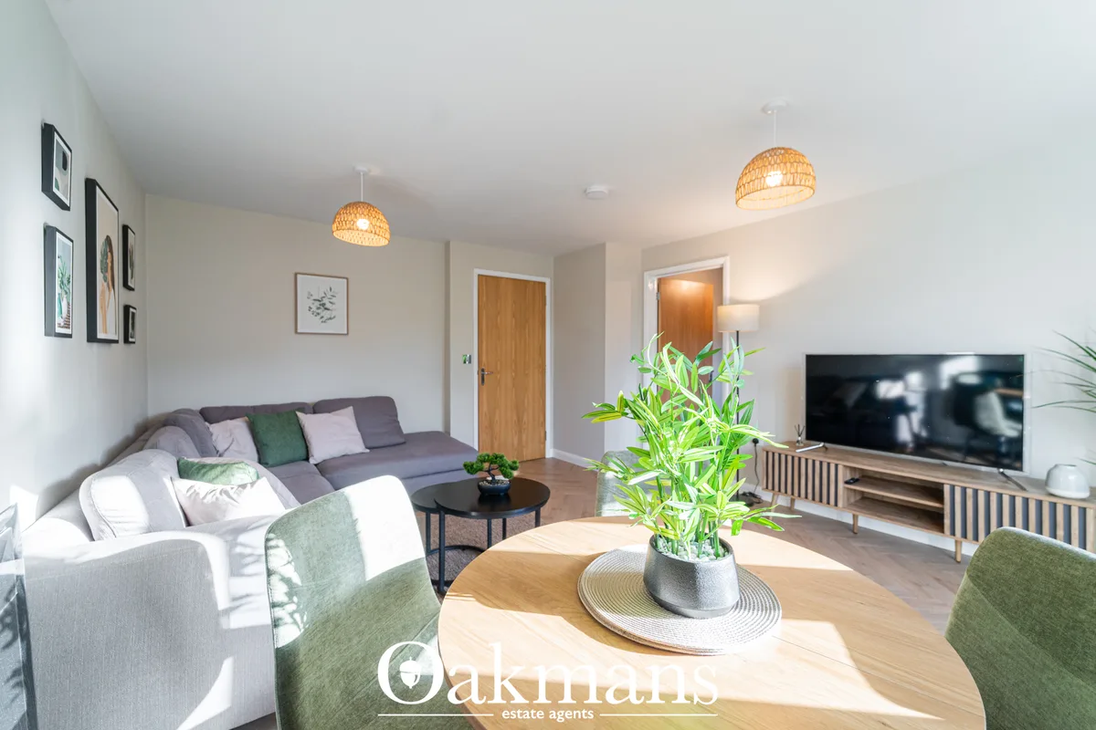 Bright open-plan living space with grey sofa, woven pendant lights, wooden dining table with potted plant, TV on sideboa