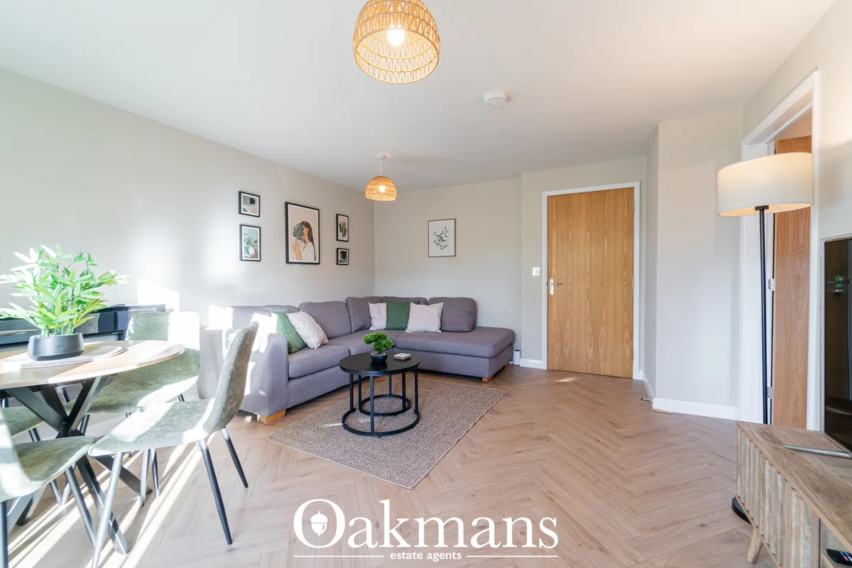 Open-plan living room with grey corner sofa, dining area, wooden flooring, pendant lighting and wall art