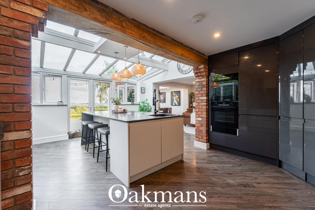 Modern kitchen with tan cabinetry, white worktops, breakfast bar, pendant lights, exposed brick, wooden beams, glazed co
