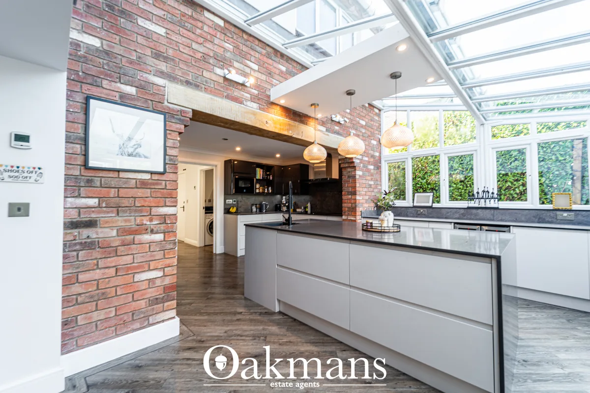 Modern kitchen with white units, dark worktops, brick feature wall, skylight roof, pendant lights and breakfast bar isla