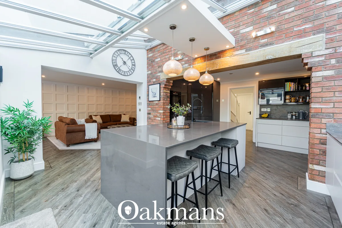Modern open-plan kitchen with grey island, black bar stools, white cabinetry, exposed brick wall and pendant lighting