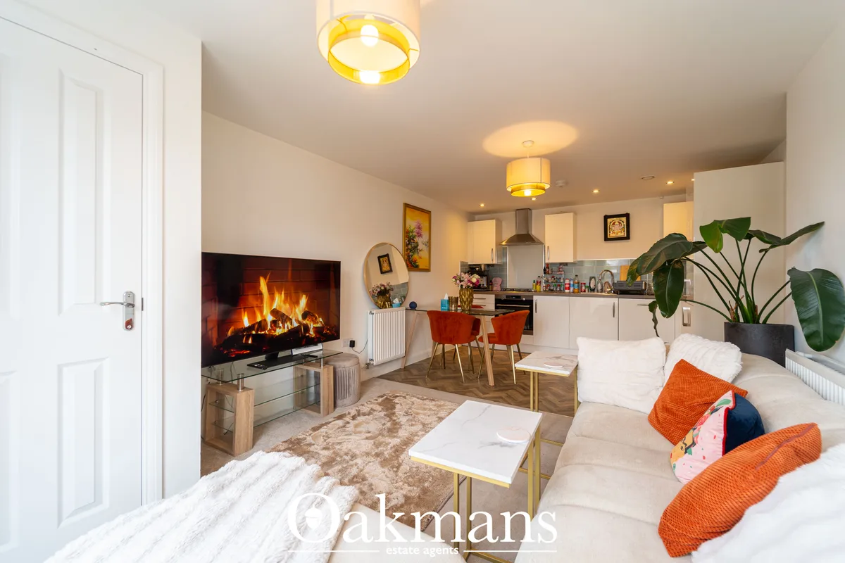 Open-plan living room with electric fireplace, cream sofa, orange cushions, dining area with wooden table and chairs, fi