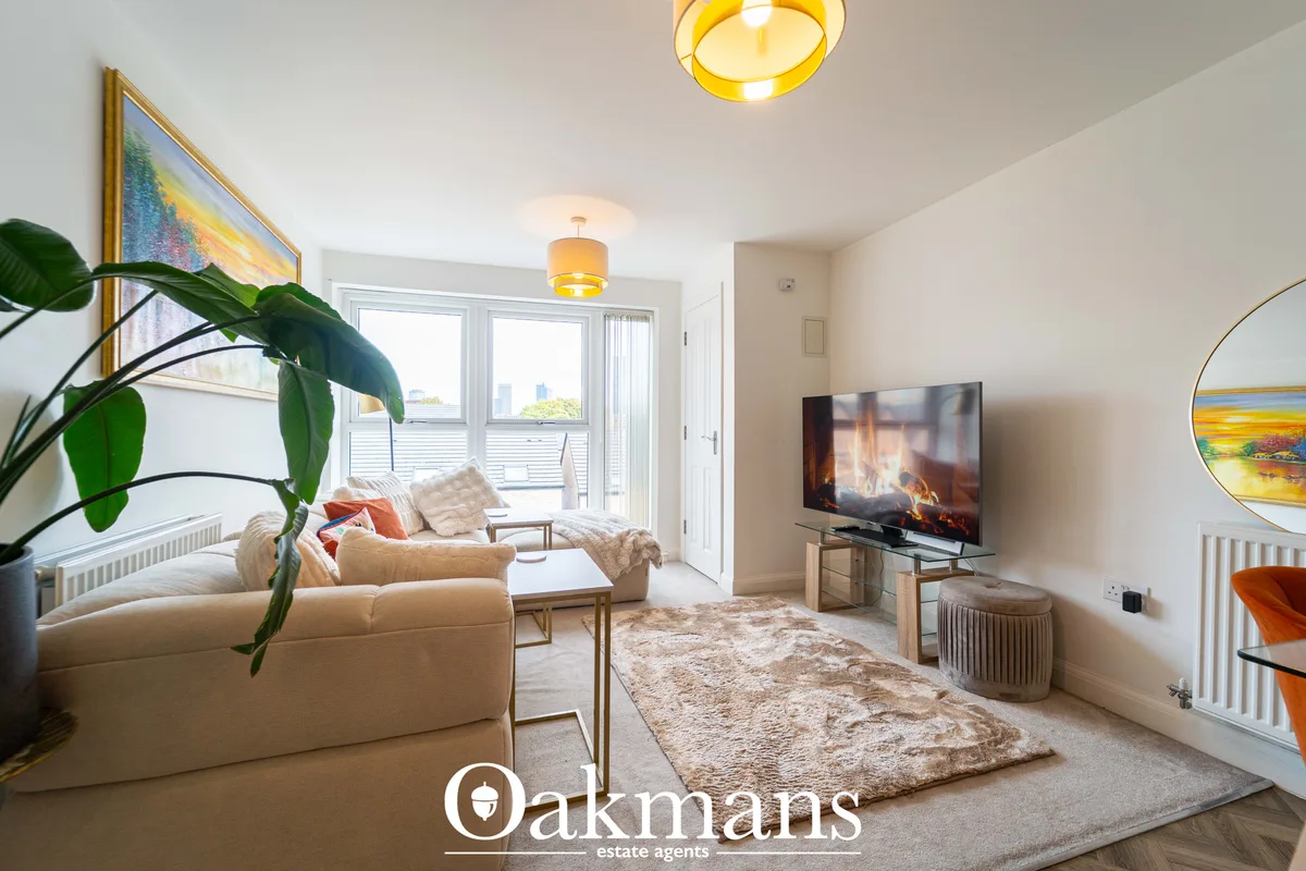 Bright living room with cream sofa, TV, framed artwork, potted plant, wooden flooring, multiple ceiling lights and balco