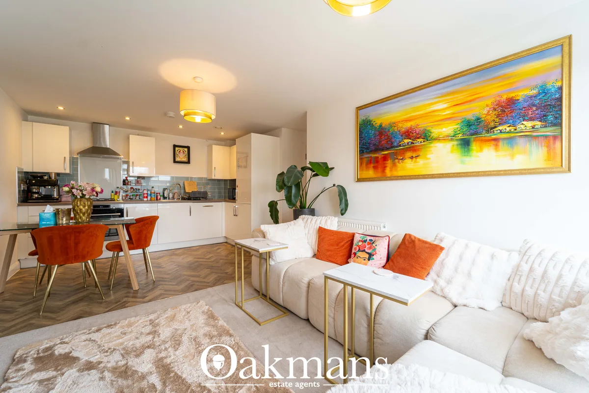 Open-plan living room with cream L-shaped sofa, orange cushions, wooden coffee table, beige rug, and large framed landsc