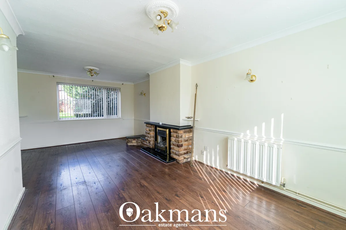 Spacious living room with cream walls, hardwood flooring, brick fireplace with brass fittings, bay window with vertical 
