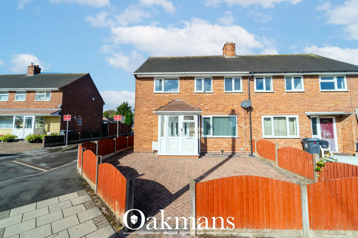 Semi-detached brick house with paved driveway, white entrance door, red fencing, and moss-covered slate roof