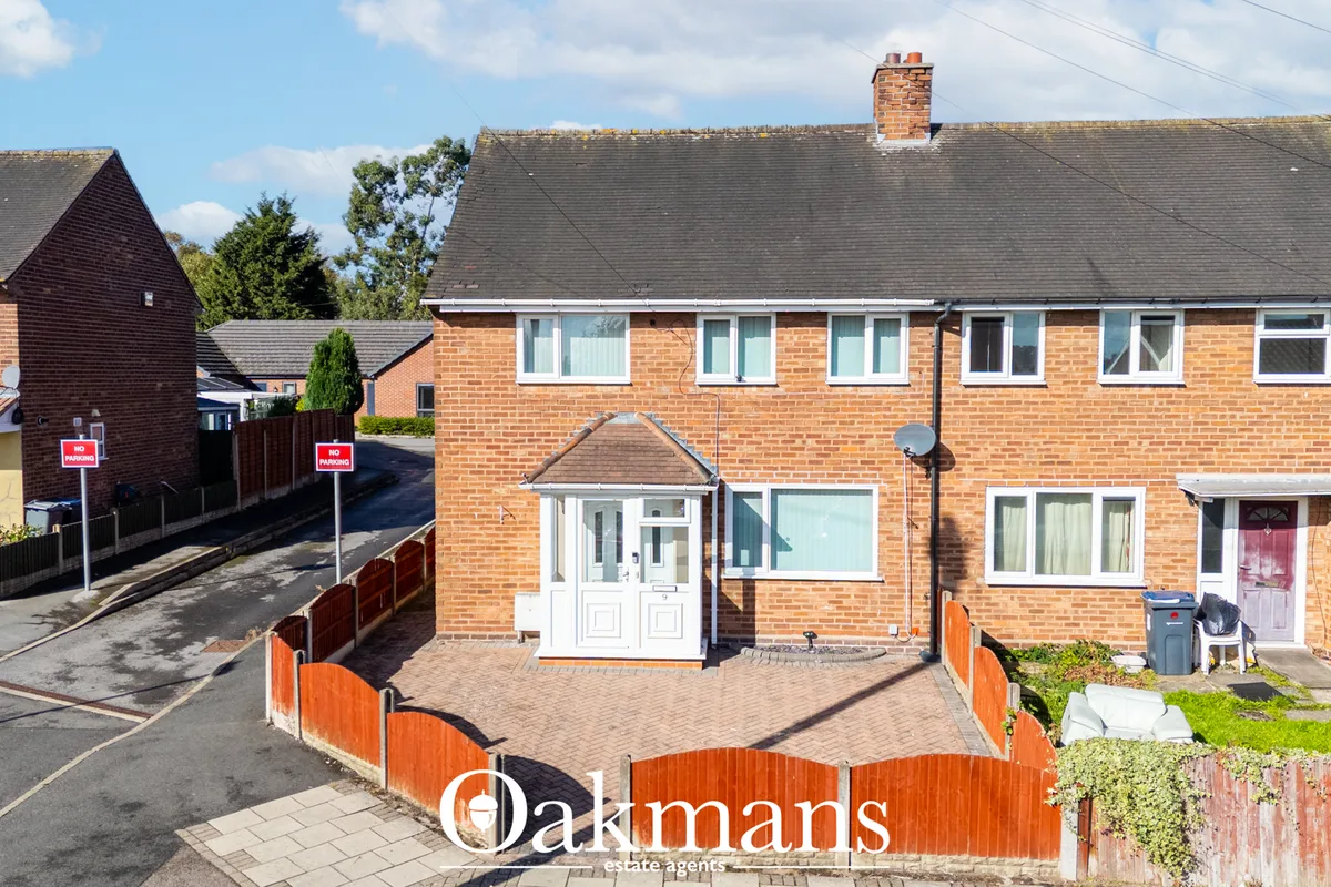 Brick semi-detached house with white PVC entrance porch, driveway and brick boundary wall under clear sky