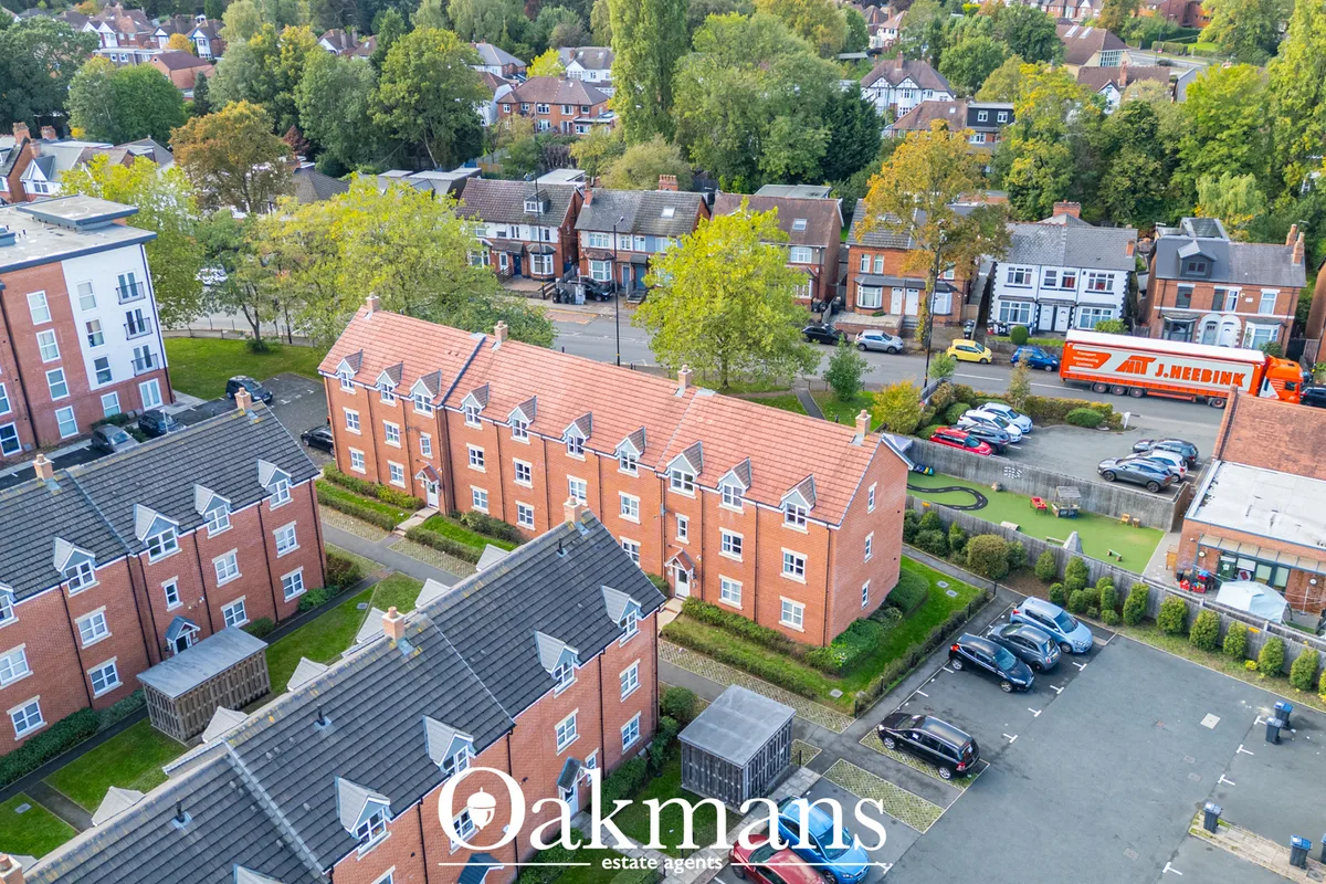 Aerial photograph of residential street with brick townhouses, parked cars, green trees and delivery van