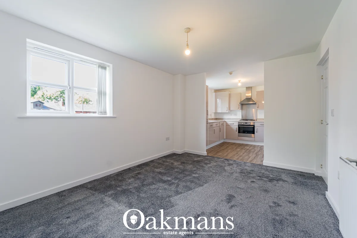 Bright living room with grey carpet, white walls, pendant light, large window overlooking garden, open-plan to kitchen
