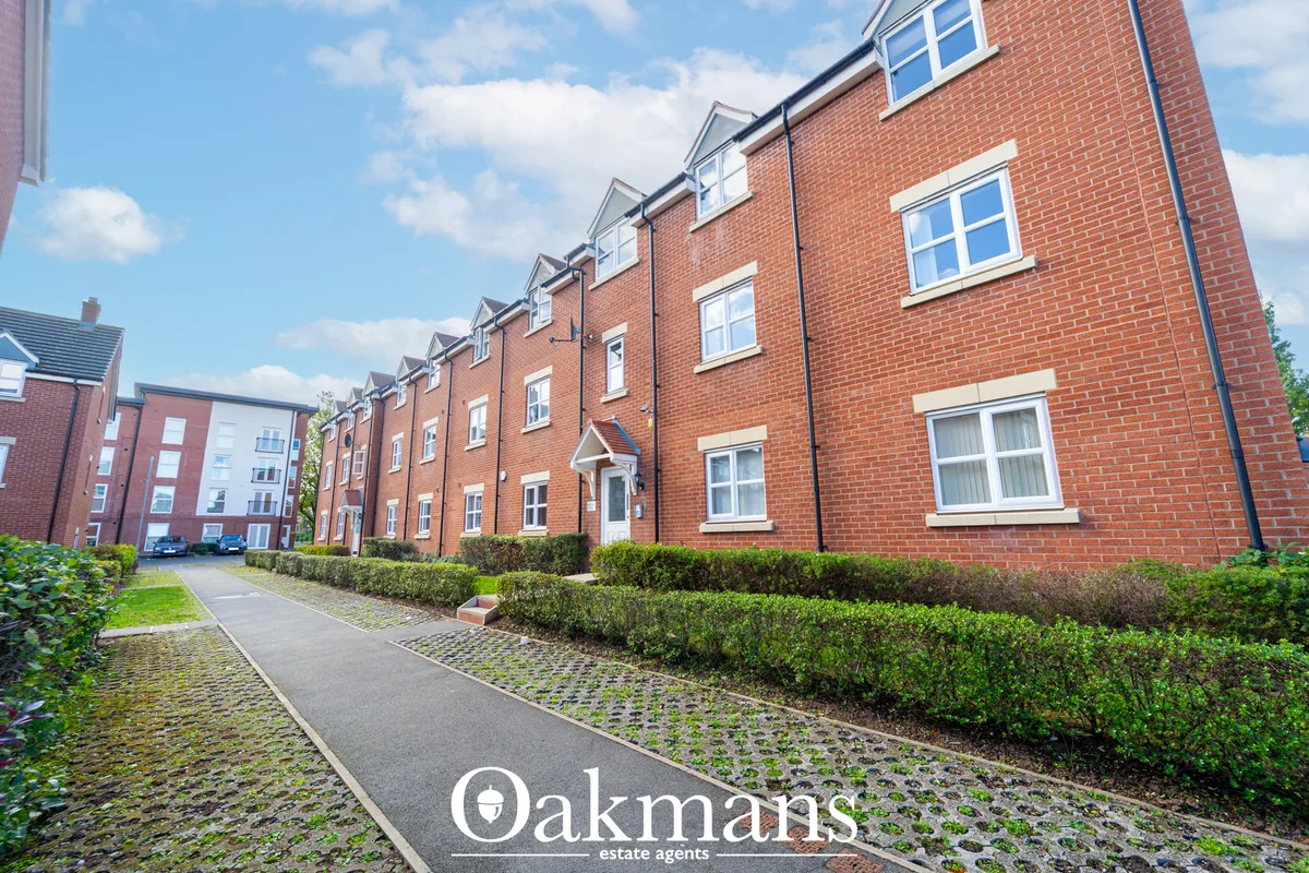 Modern red brick apartment building with dormer windows, manicured hedges and paved pathway under blue sky