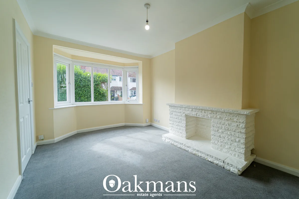 Spacious living room with pale yellow walls, grey carpet, large bay window overlooking greenery, white brick fireplace f