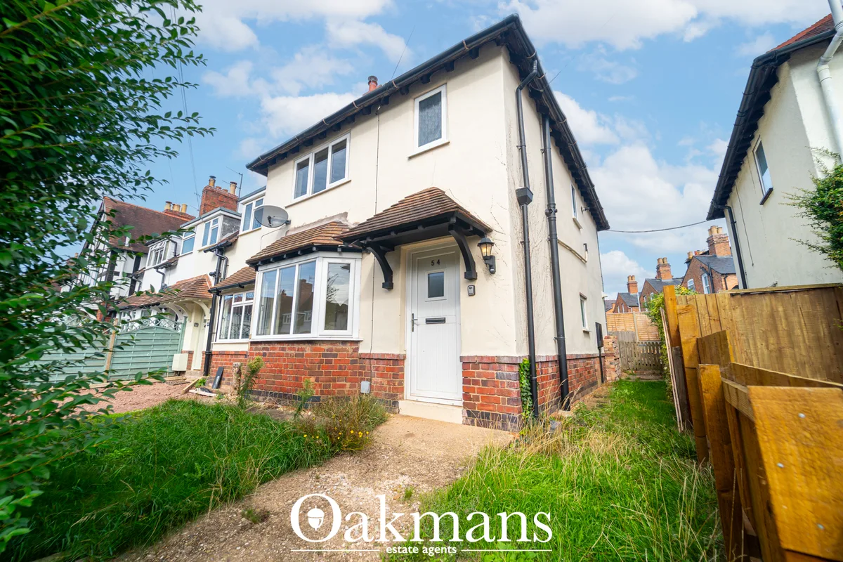 Two-storey semi-detached house with cream render and red brick base, pitched roof, front porch, gravel driveway and matu