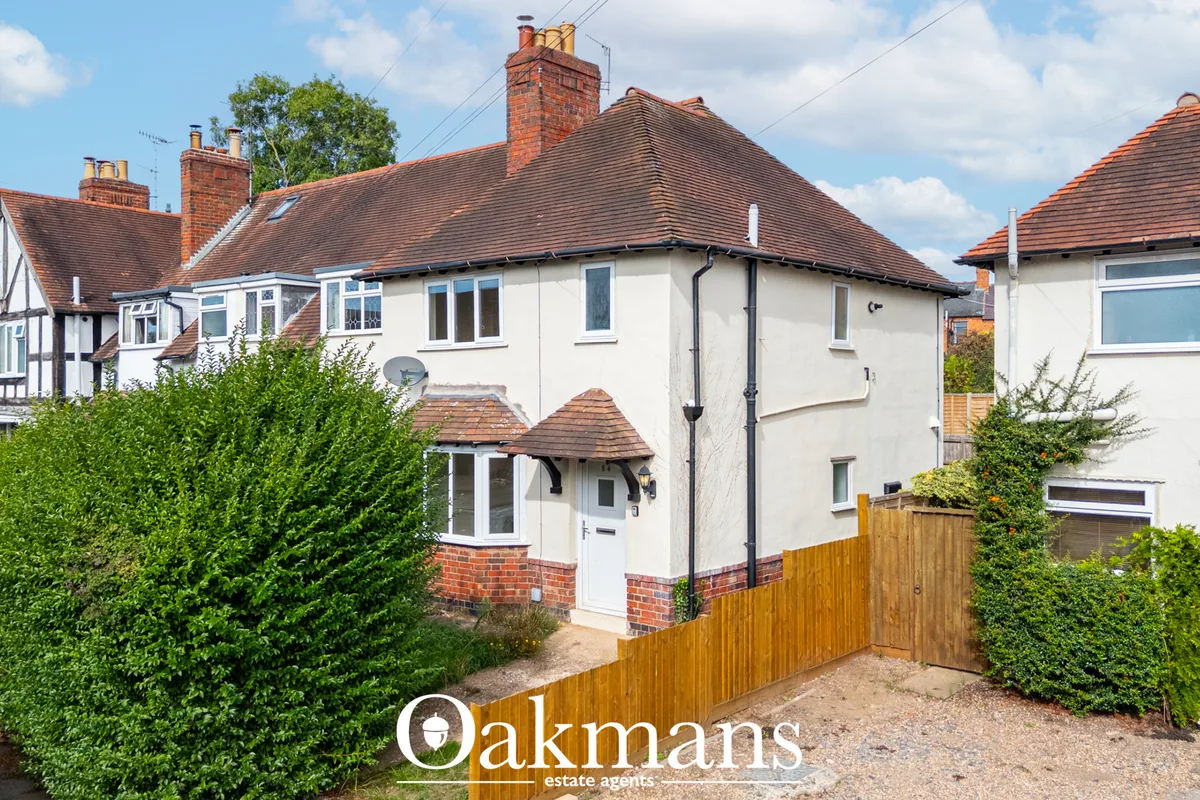 White-rendered semi-detached house with red-brick detailing, clay tile roof, wooden fence and mature hedging to front