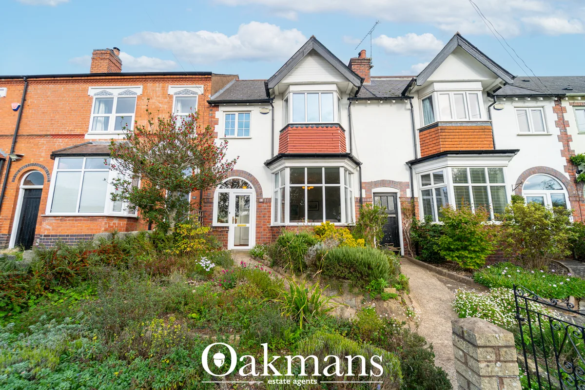 Terraced brick houses with white gable features, bay windows, orange tile roofs, and planted front gardens behind low wa