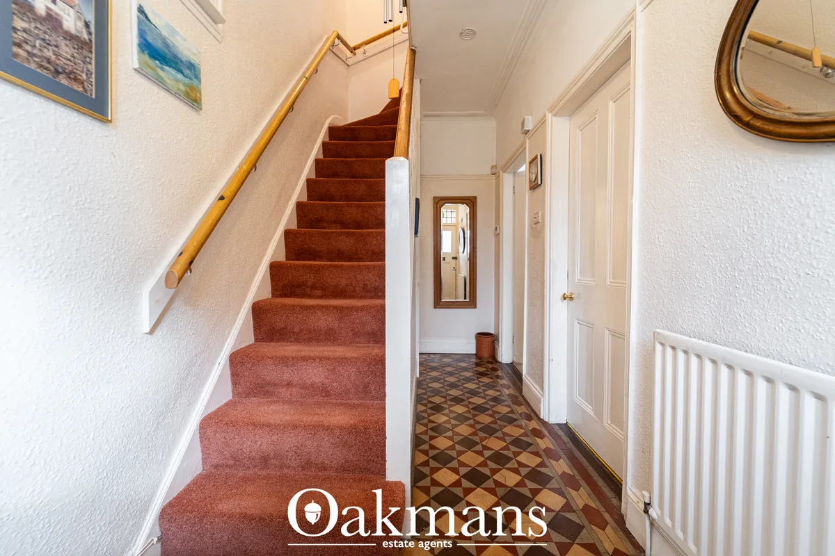Carpeted staircase with wooden handrail leading upward, cream walls, patterned tile floor, white doors, wall art and mir