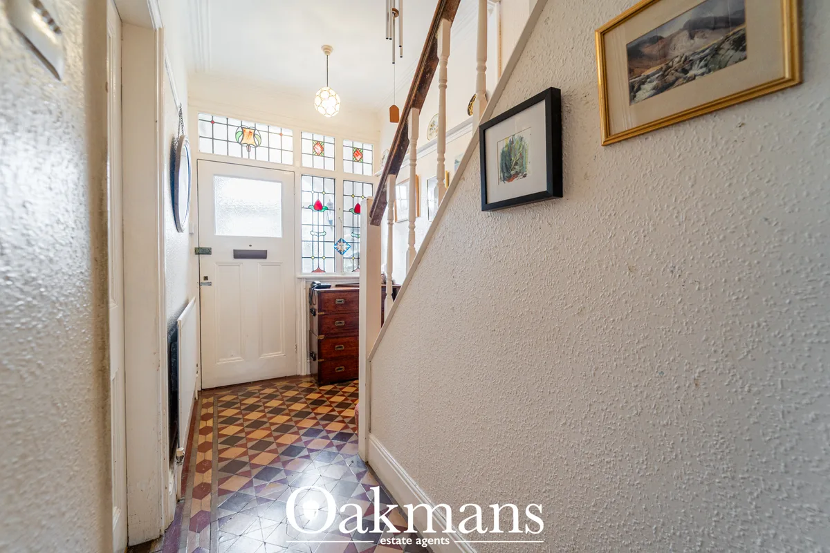 Bright entrance hallway with patterned floor tiles, cream walls, staircase with wooden handrail, white front door with s