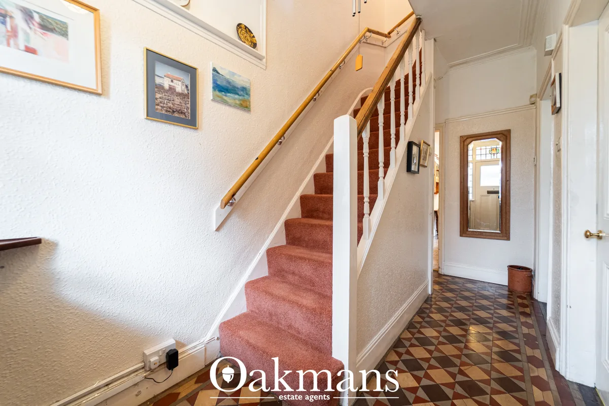 Entrance hallway with beige walls, wooden staircase with burgundy carpet, tiled floor, framed artwork, and white interio