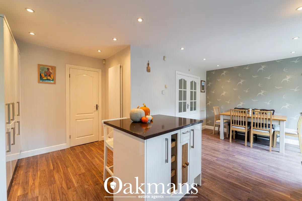 Modern open-plan kitchen with white island, black worktop, cream cabinetry, recessed lighting, and view into dining area