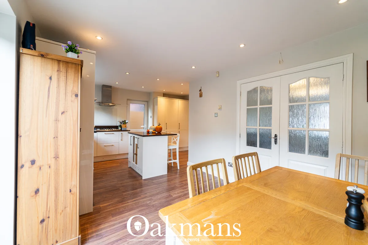 Open-plan dining room with wooden table and chairs, adjacent to modern kitchen with white units and breakfast bar