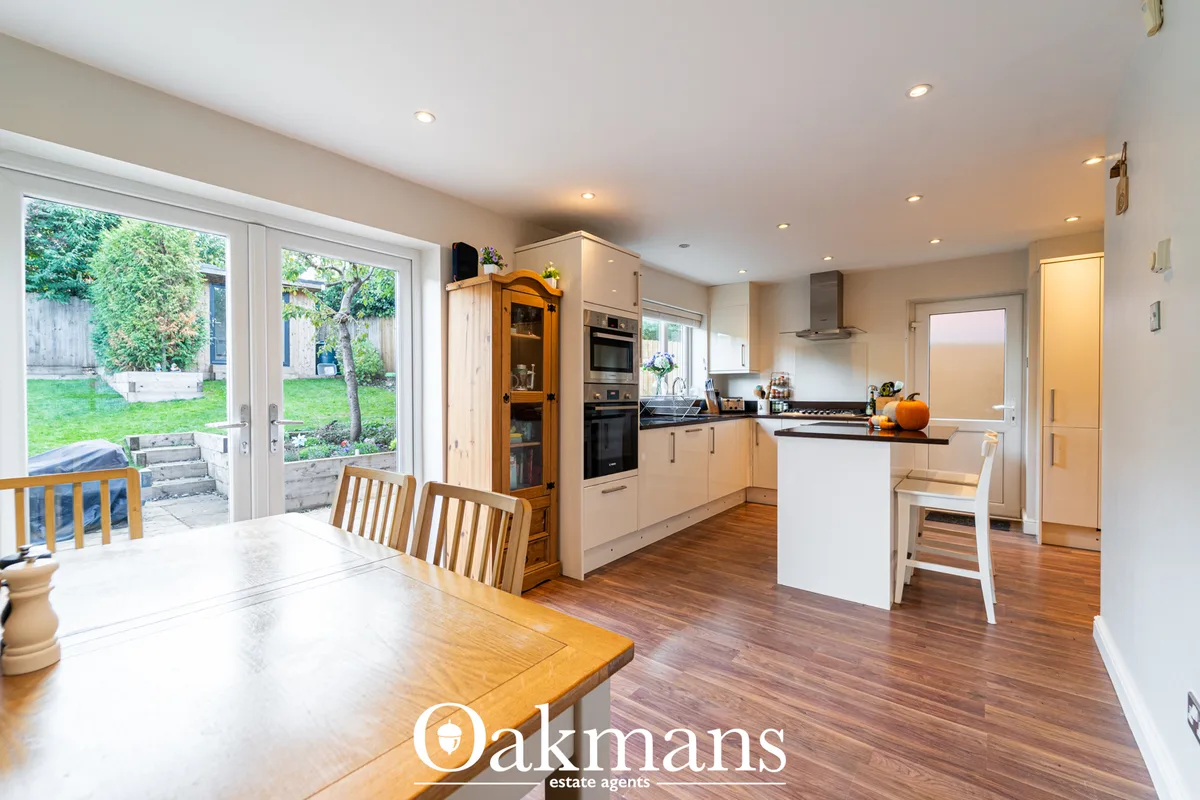 Modern open-plan kitchen with cream units, white island, black worktops, integrated appliances and wooden flooring, open