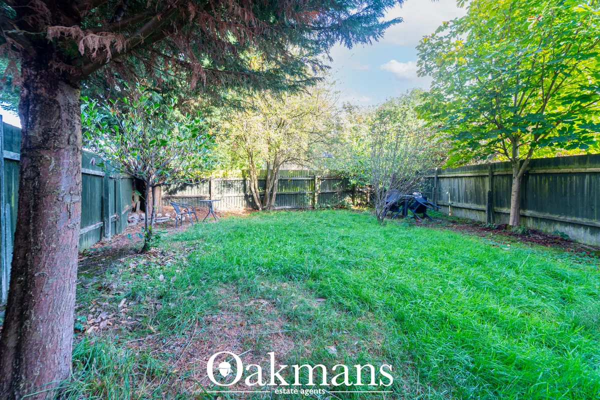Rear garden with mature trees, green lawn, wooden fencing and garden structures under blue sky
