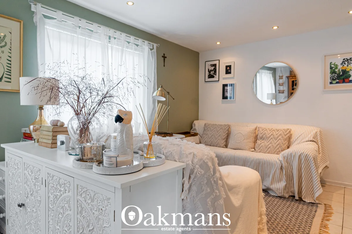 Bright living room with beige striped sofa, white ornamental cabinet, dried flower arrangements, round mirror, and large