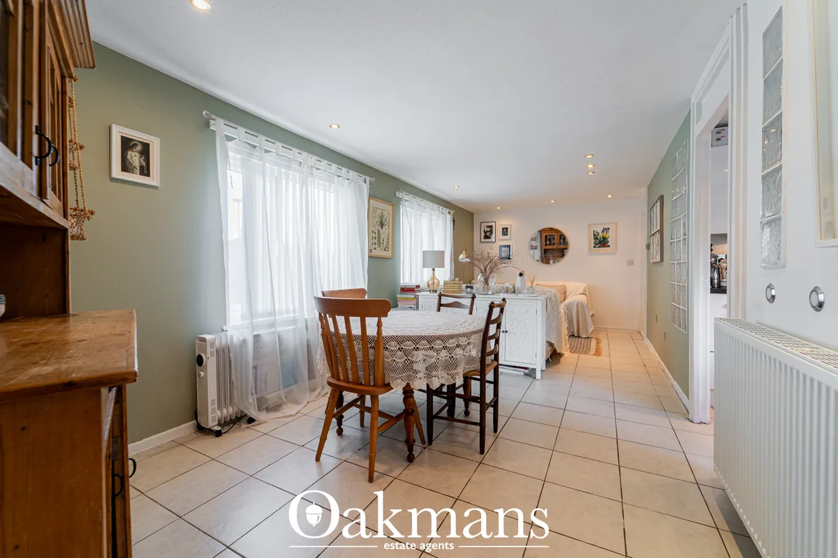 Spacious dining room with round table, wooden chairs, sage green walls, white radiator, natural light from windows and c