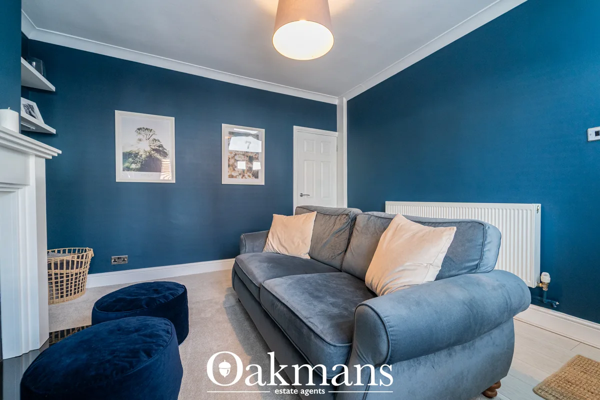 Bright living room with teal blue walls, grey upholstered sofa, navy velvet poufs, framed wall art, white ceiling light,