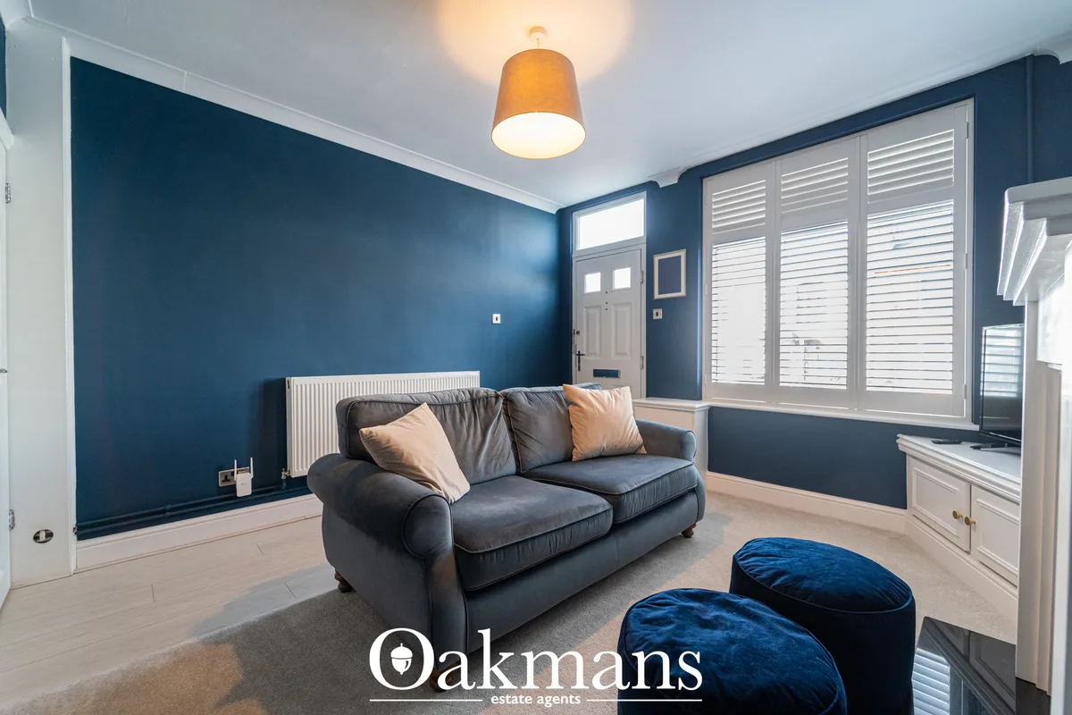 Modern living room with deep blue accent wall, grey sofa with cushions, blue velvet poufs, wooden flooring, white shutte
