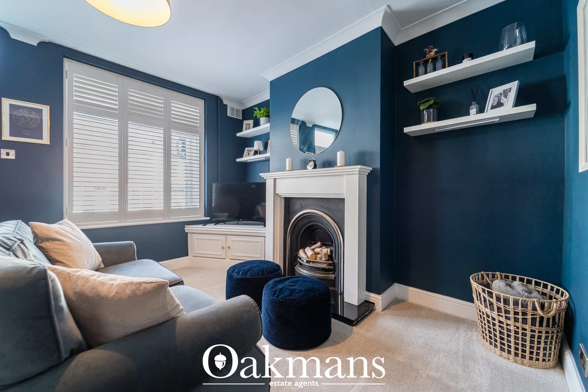 Teal living room with fireplace, white mantelpiece, round mirror, floating shelves, grey sofa, blue poufs, window shutte