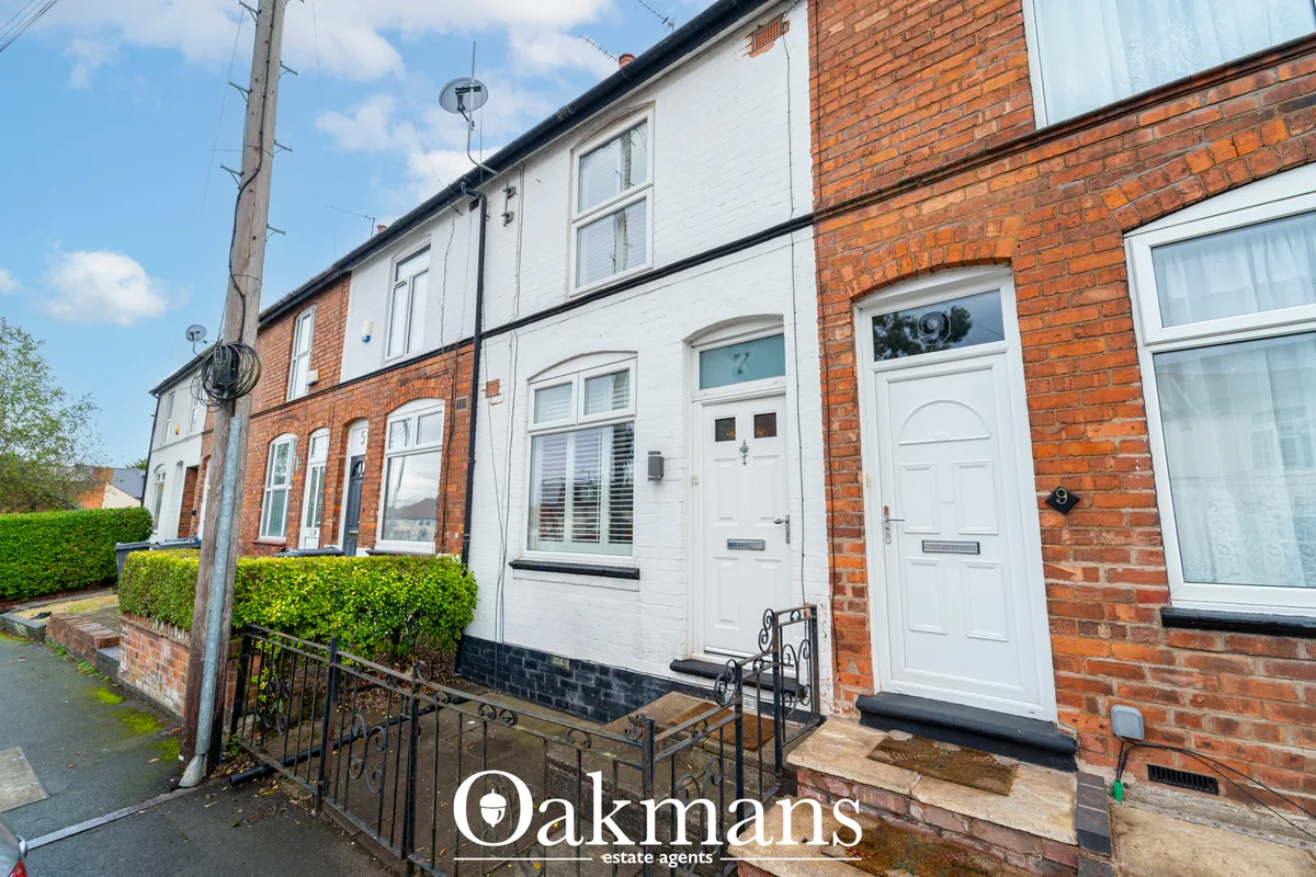Brick terraced houses with white-painted doors and windows, black railings, mature hedging, clear blue sky